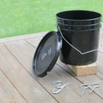 Black bucket chicken waterer with lid, base, and two pair of hooks