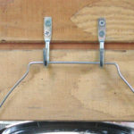 A one-gallon bucket hangs from a pair of wall hooks in a chicken coop