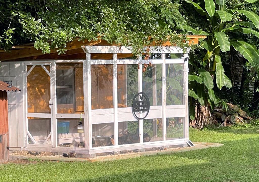 Gallinero tipo loft con acceso directo, pintado de blanco, en un frondoso jardín del sur de Alabama.