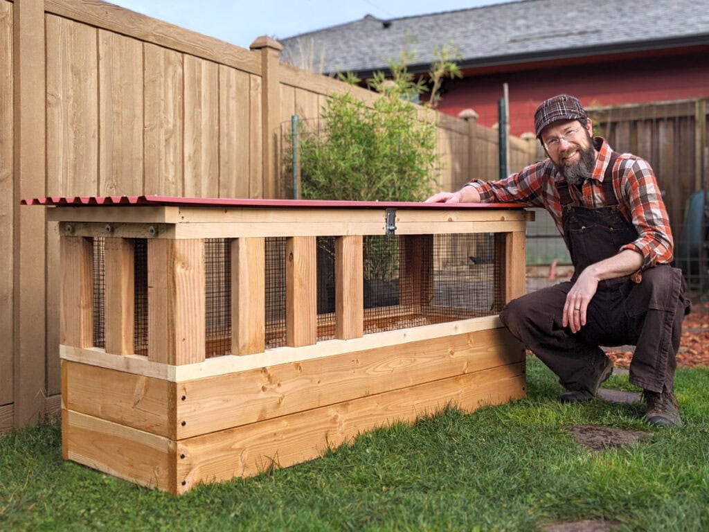 Quail keeper crouches beside The Quail Pod on-ground coop built using DIY construction plans